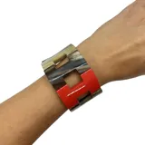 Pulsera elástica que combina eslabones en asta con detalles esmaltados en color rojo.