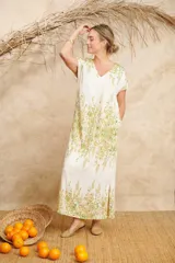 Vestido largo color blanco con estampado floral en tonos verdes y amarillos, con escote en V y mangas cortas.