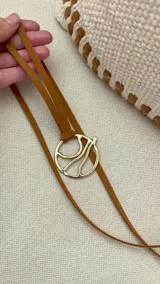 Gargantilla marrón con dije circular dorado con diseño abstracto.