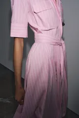 Vestido camisero midi de popelina a rayas verticales rosas y blancas, con cuello solapa, manga corta, bolsillos de parche en el pecho, cinturón de lazo ajustable y cierre frontal con botones.