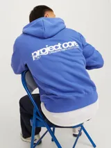 Buzo con capucha azul, de manga larga y corte holgado. Confeccionado en tejido loop back cepillado, con puños de canalé, bolsillo canguro y estampa en goma de tacto suave.