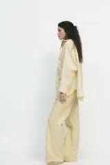 Camisa oversize a rayas amarillas y blancas, de cuello solapa y manga larga tipo murciélago acabada en puño con hombro caído. Tiene un bolsillo de plastrón en el delantero y cierre frontal con botones.