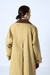 Trench color beige con cuello marrón de pana, doble botonadura y corte clásico.