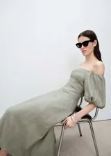Vestido midi verde oliva de lino, con escote off-shoulder y mangas cortas abullonadas. Tiene corte evasé y cierre de cremallera en la espalda.