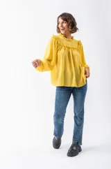 Camisa amarilla con cuello alto con volados y mangas largas abullonadas.