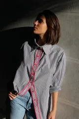 Camisa de poplin negro rayado con corte cómodo, mangas 3/4 y detalles ondeados al frente con zigzag de algodón fucsia y botones fucsia.