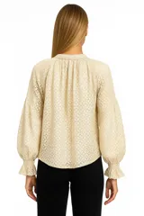 Blusa beige claro con textura calada, cuello redondo con abertura en forma de gota y mangas largas abullonadas con puños elastizados.