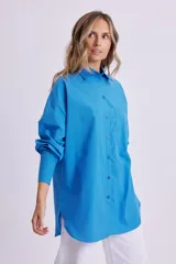 Camisa celeste de manga larga, corte oversize, con cuello clásico, cierre frontal con botones, bolsillo en el pecho y bajo redondeado.