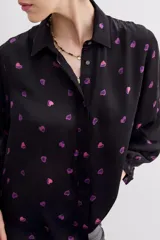 Camisa fluida negra con estampado de corazones color lila, mangas largas, cuello camisero y puños con botón.