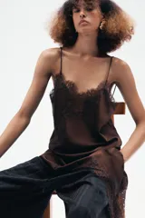 Vestido corto de satén color blanco, con tirantes finos, escote en pico y bajo asimétrico con abertura. Detalle de encaje negro en escote y ruedo.