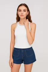 Musculosa blanca ajustada al cuerpo, sin mangas, con cuello redondo y tachas plateadas en el cuello y sisas.
