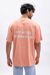 Remera de manga corta color tostado con estampado frontal en blanco que incluye texto y gráficos minimalistas.