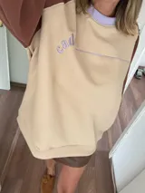 Buzo beige con mangas marrones y cuello lila, de corte holgado y largo a la cadera.