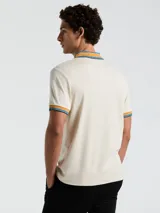 Polo manga corta color crema con cuello y puños a rayas en tonos azul y naranja.