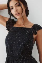 Mono corto negro con estampado de lunares blancos. Presenta escote cuadrado, breteles anchos con volados y elástico revestido en la cintura.