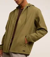 Campera rompevientos color verde oliva, con capucha ajustable con cordón, cierre frontal con cremallera, bolsillos laterales con cremallera y puños elásticos.