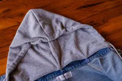 Campera de jean celeste con capucha gris de algodón desmontable, cierre con botones metálicos y bolsillos delanteros.