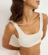 Top tipo bralette sin aros ni copas, color beige claro, con escote cuadrado y tirantes medianos. Presenta una banda inferior texturizada con doble línea horizontal.