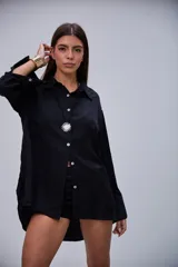 Camisa negra de manga larga, con cuello clásico y cierre frontal de botones blancos.