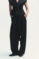 Pantalón negro con finas rayas verticales blancas, de tiro alto y corte ancho. Incluye cinturón de lazo en el mismo tejido, bolsillos laterales y pinzas.