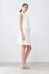 Falda corta color crudo tejida con textura acanalada horizontal y terminación desflecada en el ruedo.