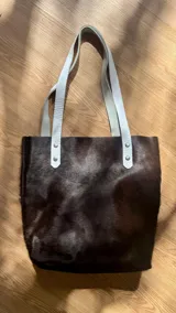 Bolso tipo tote de cuero con pelo color marrón y blanco, con manijas de cuero crudo.