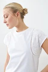 Remera blanca de algodón con cuello redondo y mangas cortas con detalle de broderie y vainillas.