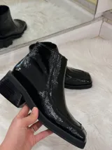 Bota de charol negra con punta cuadrada, tacón grueso y cierre lateral.