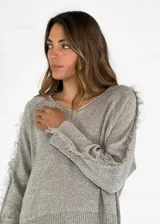 Sweater beige de tejido de punto con detalle de flecos en hombros y mangas.