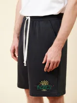 Bermuda de felpa negra con cintura elástica ajustable con cordón blanco. Presenta un estampado con un sol y el logo de la marca en la pierna derecha.