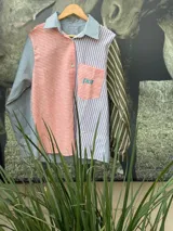 Camisa de manga larga con diseño patchwork a rayas horizontales en tonos celeste, naranja y verde. Tiene cuello clásico, bolsillo en el pecho y cierre con botones.