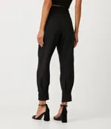 Pantalón zanahoria de crepé negro con pliegues, corte de sastrería, trabillas en la cintura y abertura con botón y cremallera.