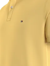 Chomba amarilla de Tommy Hilfiger, modelo 1985, de corte regular, con cuello tipo chomba, cartera de dos botones, logo bordado en el pecho y diseño de rayas en el interior del cuello.