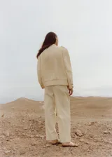 Pantalón de tiro medio color crema, de corte recto y cierre cruzado. Confeccionado en tejido mezcla de algodón y lino. Presenta dos bolsillos laterales, detalle de pinzas, bolsillo de parche en la parte posterior y cinturón ajustable.