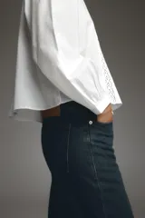 Camisa blanca de cuello subido y manga larga, con detalle de entredós combinados a tono y cierre frontal con botones.