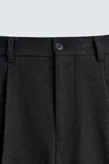 Pantalón de vestir negro, corte amplio, con pliegues en la cintura, bolsillos laterales y traseros de ojal.
