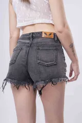 Short de jean negro lavado con efecto desgastado y roturas. Presenta apliques de strass o brillos distribuidos por toda la prenda y terminación de ruedo deshilachada.