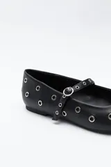 Zapato bajo tipo bailarina de color marrón oscuro, con puntera afilada y tira con hebilla sobre el empeine. El cuerpo del zapato está adornado con múltiples ojales metálicos plateados.