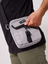 Bandolera gris de nylon con correa negra ajustable y logo Rusty estampado en negro.