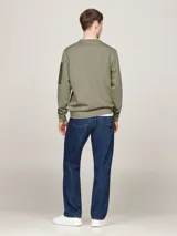 Buzo verde militar de Tommy Hilfiger, de corte clásico con cuello redondo y mangas largas. Presenta un pequeño logo bordado en el pecho y un bolsillo con cremallera en la manga izquierda.