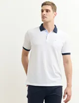 Remera polo blanca de piqué con cuello y puños en azul marino. Tiene tapeta de dos botones y bolsillo de parche en el pecho.
