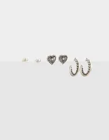 Set de tres pares de aros plateados: un par de aros tipo botón, un par de aros con forma de corazón y un par de aros tipo argolla con diseño trenzado.