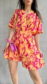 Vestido corto de color naranja con estampado floral en tonos fucsia y amarillo, con mangas abullonadas.
