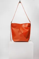 Bolso tipo bucket de cuero color marrón con costuras a la vista, doble bolsillo interior (uno con cierre) y correa regulable.