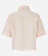 Camisa color beige claro, corta, con cuello inglés, manga corta, bolsillo en el pecho y abotonada adelante.