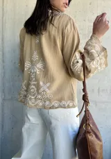 Chaqueta color beige con bordados blancos en el frente y las mangas, de corte recto y mangas anchas.