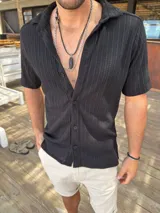 Camisa negra tejida con textura acanalada, de corte clásico, manga corta y cuello camisero.