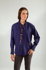 Camisa azul con cuello mao con volados, manga larga con puños con volados, cierre frontal con botones y bolsillo de parche con broche decorativo en forma de insecto.