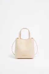 Bolso tote pequeño de cuero sintético color negro con doble asa de mano y correa bandolera ajustable y extraíble. Logotipo de la marca en letras doradas en la parte frontal.