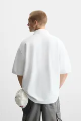 Polo blanco de piqué con corte relaxed fit, cuello solapa y cierre frontal con botones.